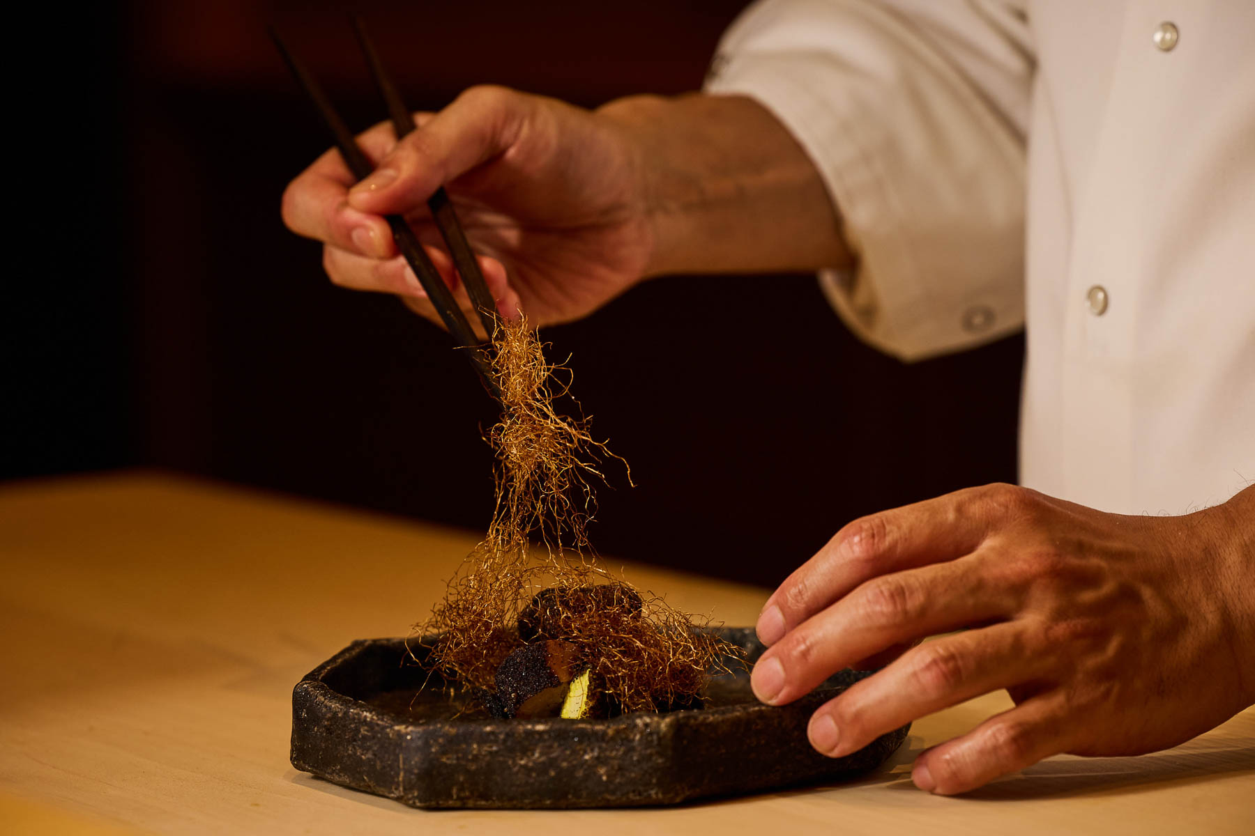 Chef preparing a Japanese fine dining dish by hand.